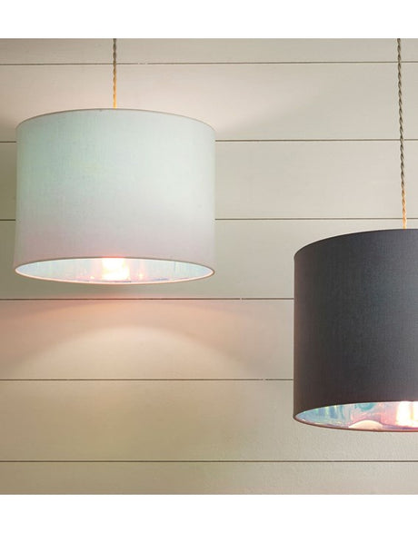 A picture of a pale cream coloured lampshade taken against a pale background with horizontal panels. The lampshade is hanging from a grey twisted cable. To the right of the picture a grey coloured lampshade can also be seen but is slightly cropped out of the image.
