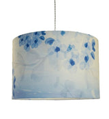 Straight sided cylinder pendant lampshade with a blue printed blossom and leaf pattern, hanging from a pale grey coloured twisted cable taken on a white background.