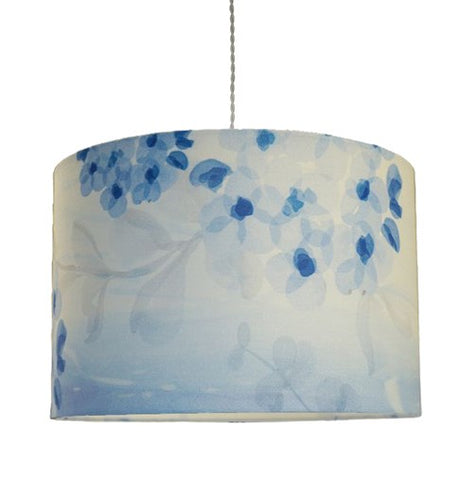 Straight sided cylinder pendant lampshade with a blue printed blossom and leaf pattern, hanging from a pale grey coloured twisted cable taken on a white background.
