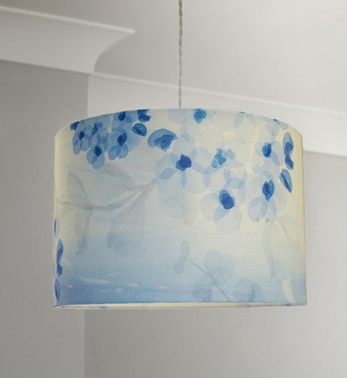 Straight sided cylinder pendant lampshade with a blue printed blossom and leaf pattern, hanging from a pale grey coloured twisted cable in a room with pale grey walls and white cornice.