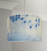 Straight sided cylinder pendant lampshade with a blue printed blossom and leaf pattern, hanging from a pale grey coloured twisted cable in a room with pale grey walls and white cornice.