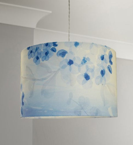 Straight sided cylinder pendant lampshade with a blue printed blossom and leaf pattern, hanging from a pale grey coloured twisted cable in a room with pale grey walls and white cornice.