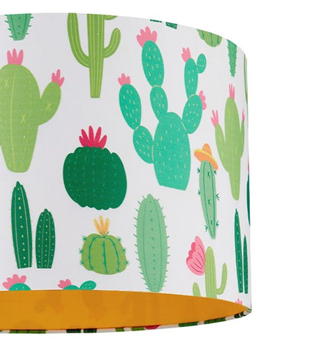 A close up picture of a straight sided white cotton cylinder lampshade that is covered in printed cartoon style illustrations of various different types of cactus plants. Some are dark green with ink flowers, some are pale green with orange flowers. Once of the cactus plants is wearing an orange coloured sombrero style hat. The lampshade has an orange coloured fabric lining.