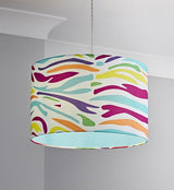 A zebra printed straight sided cylinder lampshade in fashion colours. The zebra stripes are printed in purple, yellow, green, orange, turquoise and fuchsia pink. The inside of the lampshade is lined in turquoise fabric. The shade is hanging from a grey twisted cable in a room with pale grey walls and white cornice.