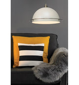 A retro looking cream metal ampshade hanging on a grey coloured twisted ceiling cable. The dome shaped lampshade has a brushed copper coloured ring approximately 2.5cm or 1 inch from the bottom. The lampshade is shown hanging low above a dark coloured fabric armchair with a fur throw over one side and a large yellow and small black and white cushion.