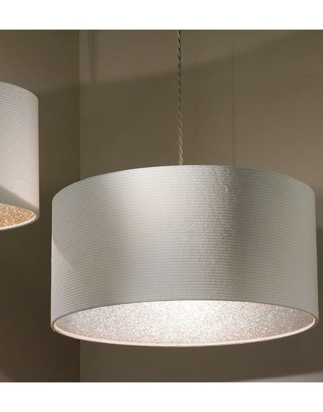 A large cylinder lampshade with a ribbed texture and just visible lining in silver glitter. The lampshade is hanging from a grey twisted cable and is taken against a beige background. A small section of another lampshade can be seen on the lefthand side of the image.